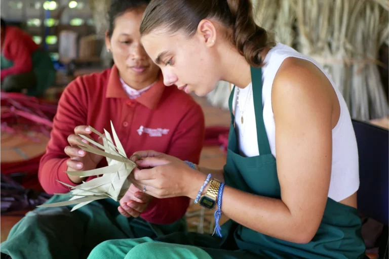 A young woman is leaning how to make a box from palm leaves with the help of Senteurs d'Angkor artisan.