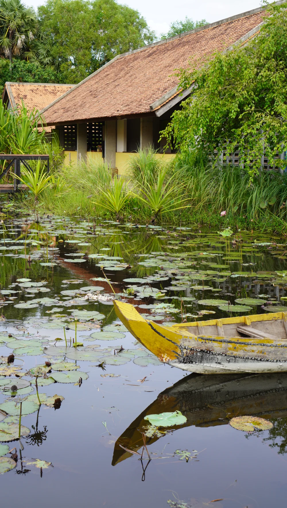 A wooden boat is floating on a pond at Senteurs d'Angkor Workshop and Garden.