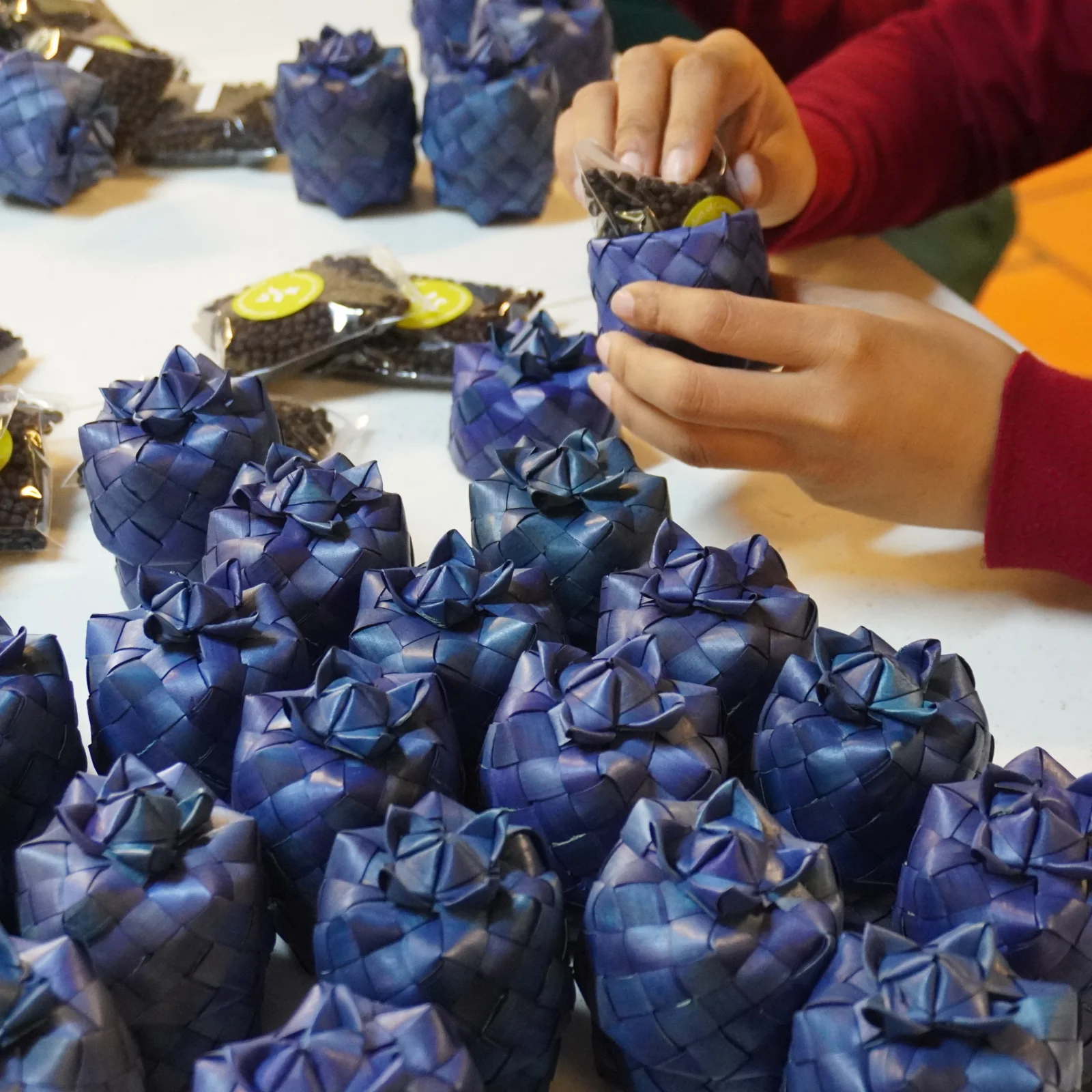 Hands of a packager filling Kampot black pepper then packing it inside a blue smok natural packaging made from sugar palm tree.